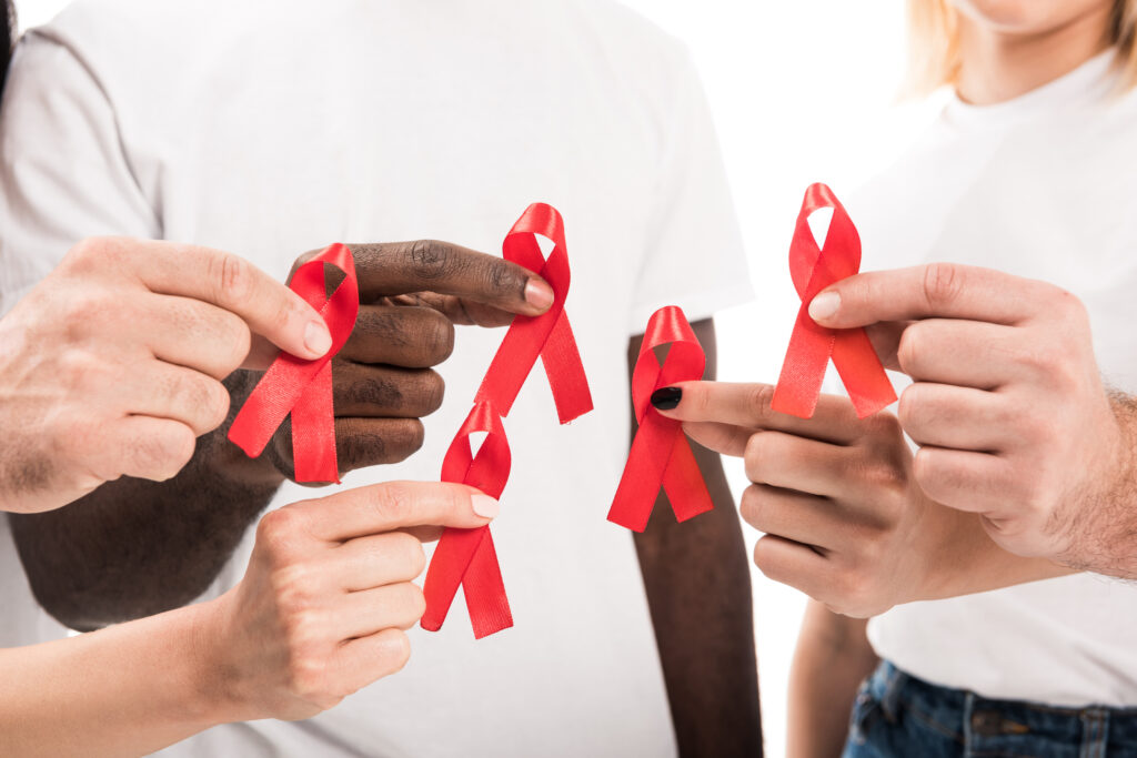 Color group photo of an ethnically diverse group of people in white t-shirts holding up red AIDS ribbons.